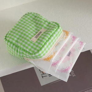 Detail view of green and white checkered cotton pouch storing sanitary napkins with zipper