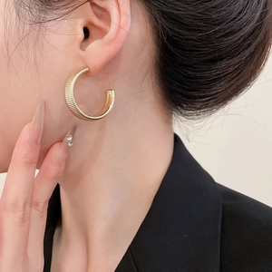 Close-up of golden C-shaped earring with striped texture worn by a model on her ear