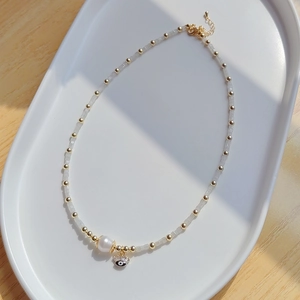Détail du pendentif œil protecteur et perle d'eau douce sur collier perlé élégant