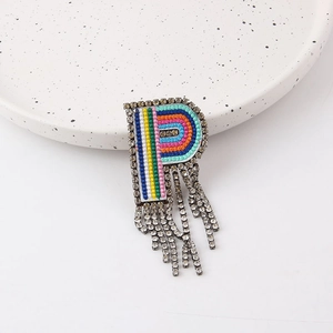 Close-up of letter R brooch with colorful embroidery, rhinestones and fringe tassels