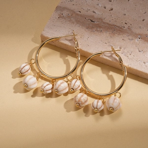 Detailed view of gold hoop earrings with white marble-textured pumpkin beads on stone