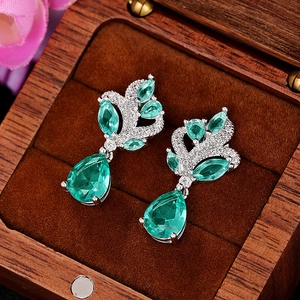 Detailed macro shot of green teardrop gems in silver leaf settings inside a wooden box