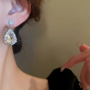 Detailed close-up of a silver teardrop earring with sparkling pavé crystals on a model
