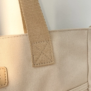Detail shot of beige canvas tote bag with woven strap and reinforced X-shaped stitching