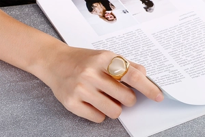 Close-up of a bold gold heart ring with beige gemstone worn on a model hand