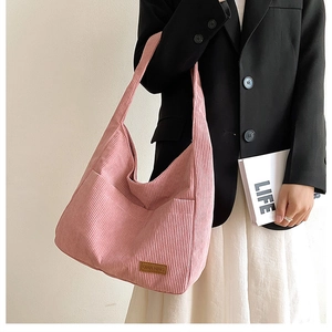 Pink corduroy shoulder bucket bag with logo tag shown in a stylish minimalist setting
