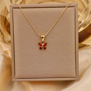 Detailed close-up of a gold bead necklace featuring a dainty red zircon butterfly pendant