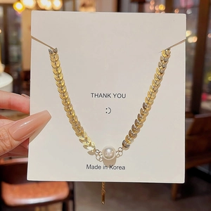 Macro detail of gold wheat leaf chain necklace with a single white pearl on a display card