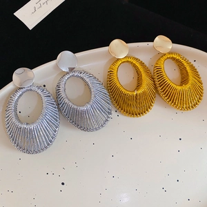 Vue détaillée de boucles d'oreilles ovales tissées en métal doré et argenté sur plateau