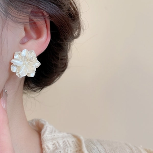 Dettaglio di un orecchino a fiore bianco con petali perlati su una modella