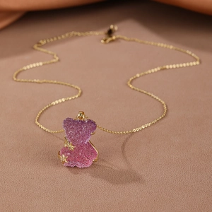 Detailed view of a gradient purple and pink resin bear pendant on a gold chain necklace