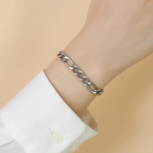 Detail showing a silver Figaro link chain bracelet worn with a crisp white shirt cuff