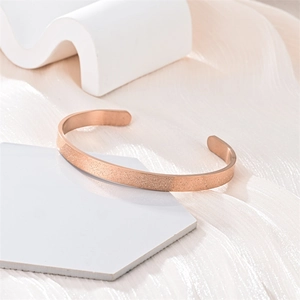 Primer plano de un brazalete de oro rosa mate en forma de C sobre soportes elegantes