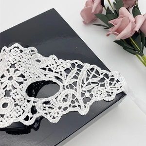 Detailed close-up of white lace masquerade mask with intricate patterns on a gift box