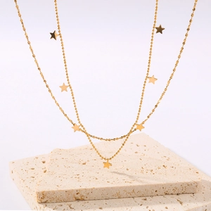 Layered 18k gold plated star pendant necklace displayed on beige stone props