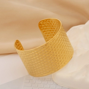 Macro shot of gold wide open cuff bracelet featuring an intricate woven metal texture