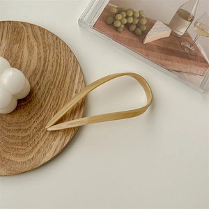 Macro detail of a beige U-shaped acetate hair pin on a wooden tray with a bubble candle