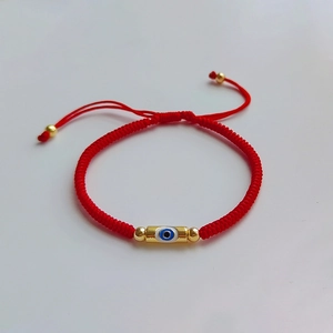Detailed shot of red woven bracelet featuring a golden evil eye charm and adjustable closure