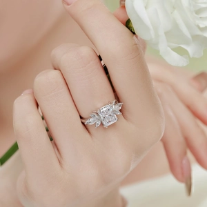 Detail of Radiant Cut engagement ring on hand with white roses and silver band