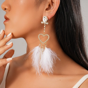 Detailed view of long gold tassel earrings with white feathers and heart rhinestones