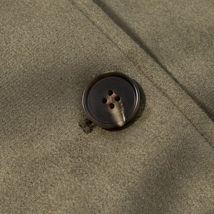 Gros plan sur la texture du daim vert olive et d'un bouton marron foncé à quatre trous