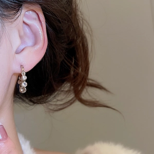 Close-up of elegant gold hoop earrings with three cascading zircons on a female model