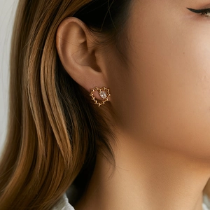 Close-up of golden heart-shaped stud earring with marquise-cut crystal on ear lobe