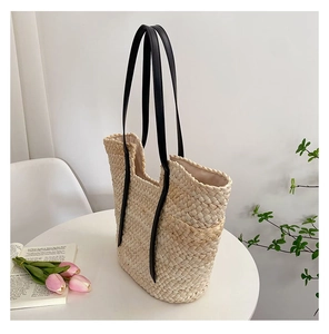 Détail d'un sac cabas en paille tissée crème avec des anses contrastées en cuir noir chic