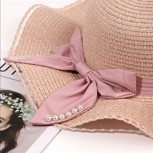 Detail of pink straw sun hat featuring a large satin bow with pearl beads and lace trim