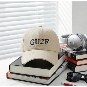 Detailed close-up of beige vintage baseball cap with black GUZF embroidery and distressed holes