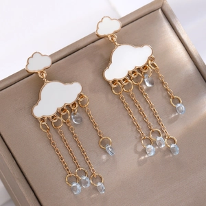 Elegantes pendientes de nube blanca con borlas doradas y gotas de cristal azul en un joyero