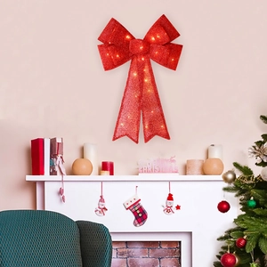 Large red LED Christmas bow with glitter finish mounted above a cozy indoor fireplace