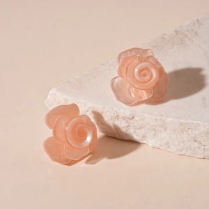 Macro shot of 3D carved pearlescent resin flower earrings on a textured stone