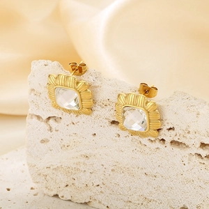 Macro shot of 18k gold plated stud earrings with square gemstone on travertine stone