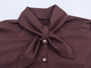 Detail of a dark brown long-sleeved blouse with a tie-neck bow and gold-rimmed buttons