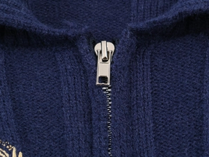 Detail shot of a silver metal zipper on a navy blue knit wool texture polo shirt