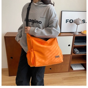 Detail einer großen orangefarbenen Canvas-Umhängetasche mit Seitentasche und Logo