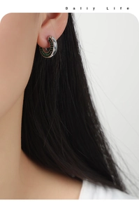 Detailed view of silver U-shaped hoop earrings with green zircon stones on a model ear