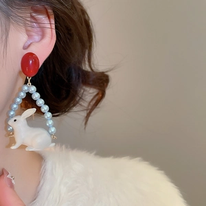 Détail de boucles d'oreilles rouges avec perles bleues et pendentif lapin blanc