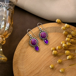 Macro shot of vintage purple marble stone earrings with teardrop crystal on a wooden tray