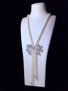 Macro view of long pearl sweater necklace featuring a sparkling crystal bow clasp