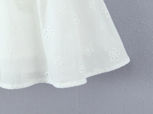 Detail of white cotton fabric featuring intricate floral embroidery and hollow-out eyelets