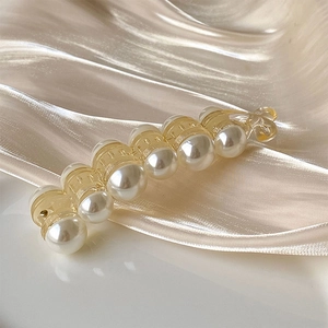 Macro detail of acrylic banana clip featuring elegant large white pearls and a golden sheen