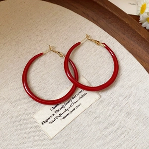 Detail of red oversized circular hoop earrings on a textured linen background