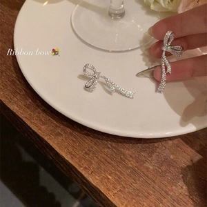 Macro view of silver ribbon bow earrings with micro-set zircons held by a hand