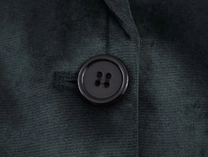 Détail macro du velours côtelé vert foncé avec un bouton noir en résine à quatre trous