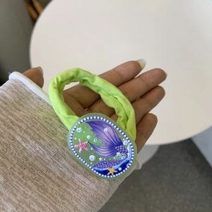 Detail of green scrunchie featuring a resin mermaid tail and starfish with colorful patterns