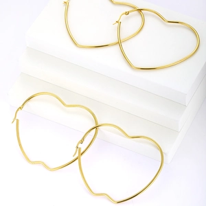 Detail view of large gold-plated heart-shaped hoop earrings on a minimalist white stand