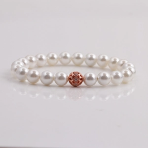 Elegant white pearl bracelet with a rose gold hollow filigree charm on a white surface