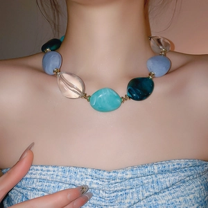 Close-up of a necklace with oval acrylic beads in blue and green on a model
